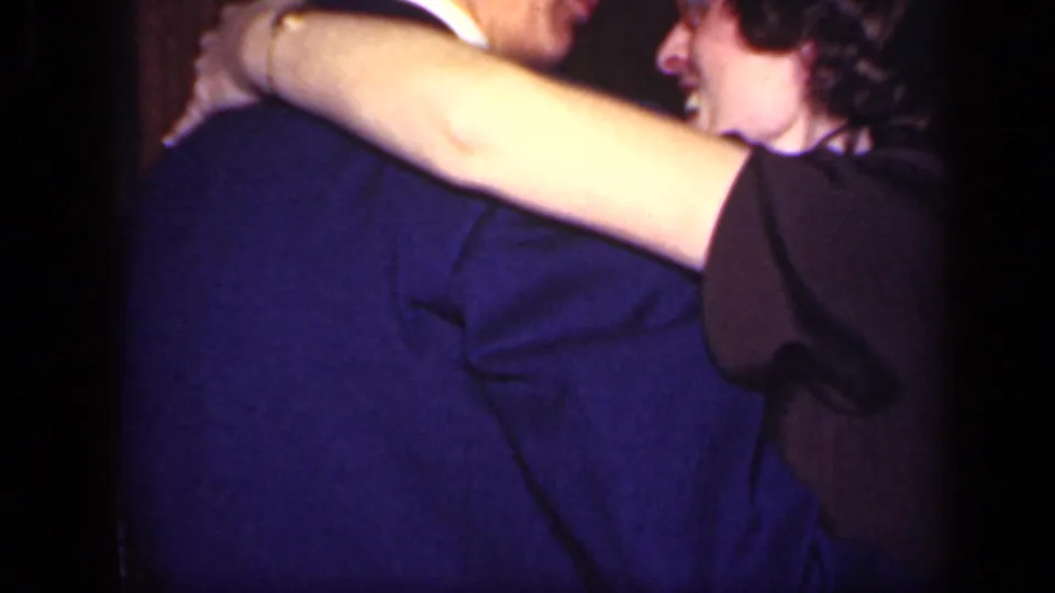 A smiling woman holds a suited man around the shoulders during close indoor dancing in supported 1949 New York footage.