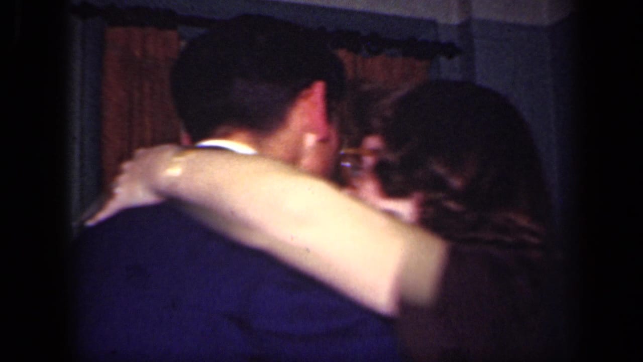 Woman wraps an arm around a man's shoulder during a close embrace indoors.