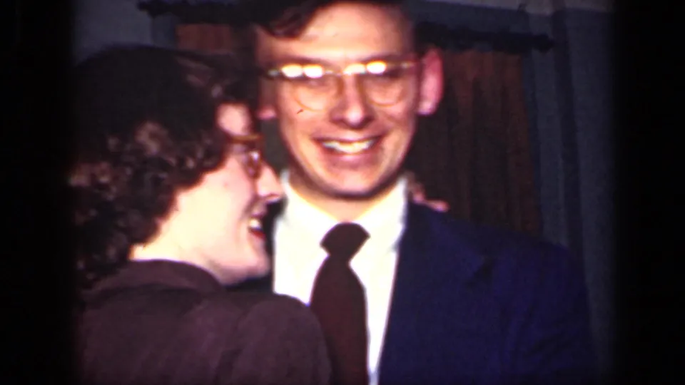 In this 1949 New York home-movie frame, a smiling man in glasses and tie stands close to a woman in a dark dress.