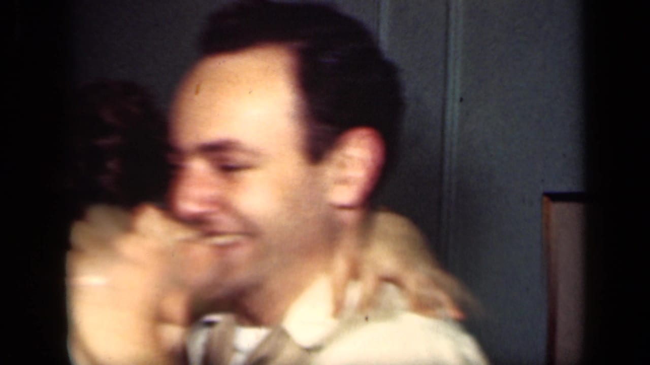A smiling man in a white shirt leans toward a woman whose arm is around his neck in the 1949 New York indoor scene.