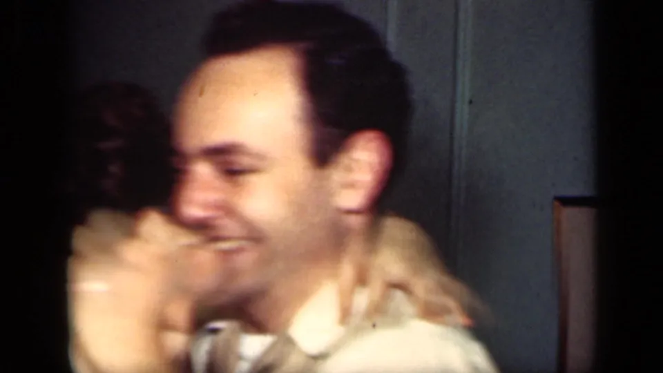A smiling man in a white shirt leans toward a woman whose arm is around his neck in the 1949 New York indoor scene.