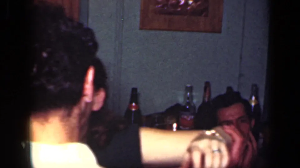 1949 New York home-movie frame showing a man from behind at an indoor gathering, with bottles and seated adults in the background.