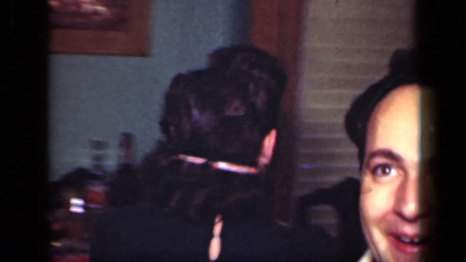 1949 New York home-movie frame showing adults crowded in a private interior, including a partially visible face near the lens.