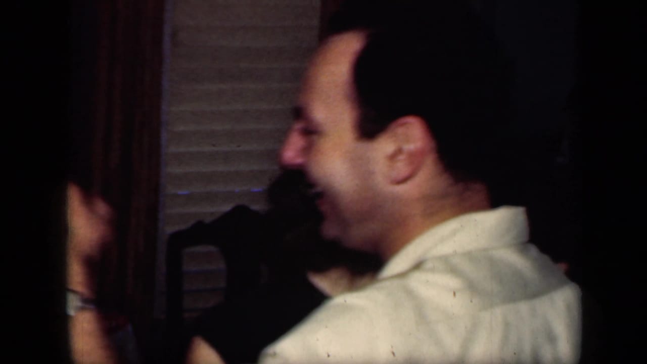 Man in a light shirt dances beside a partially visible woman in a dim interior.