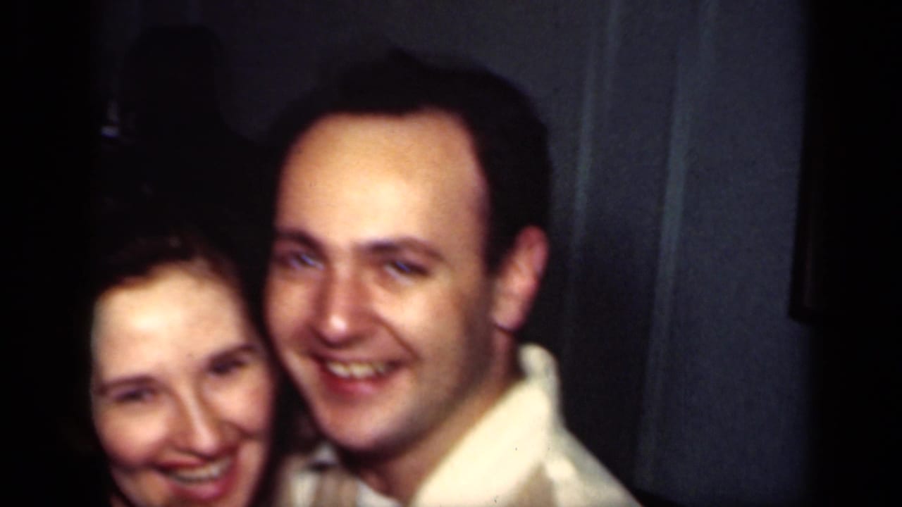 Smiling couple faces the camera while standing close together indoors.