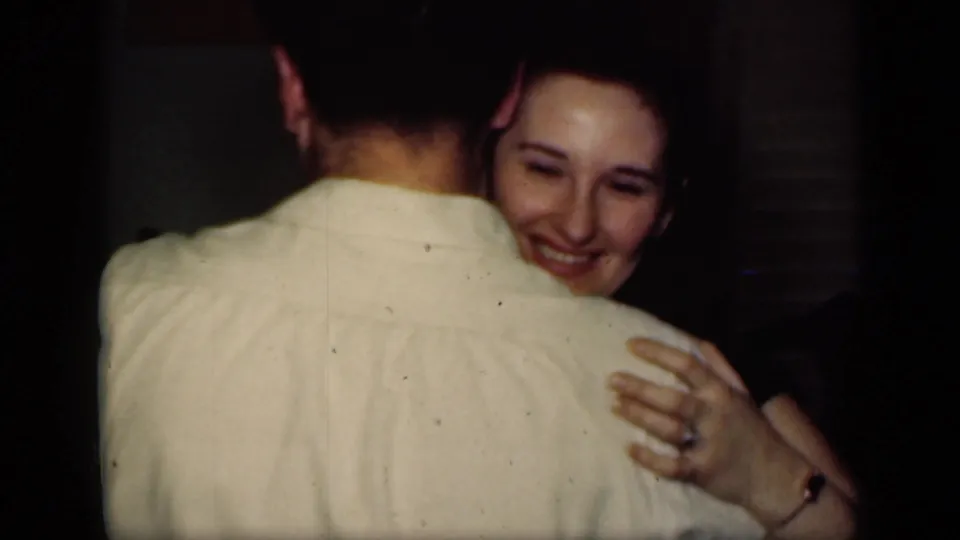A woman smiles over her partner's shoulder as they dance closely in a New York private interior recorded on 8mm film.
