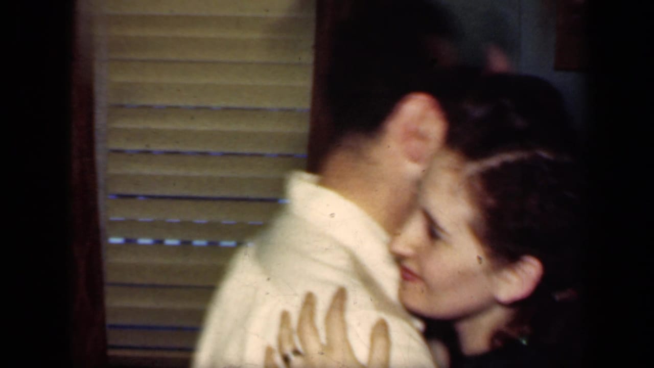A young woman embraces a man near window blinds in 1949 New York archival home-movie footage.