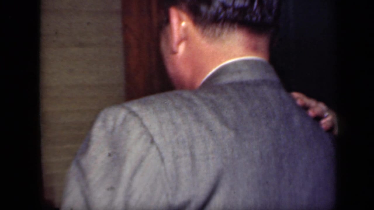 Back of a man in a gray suit dancing closely indoors.