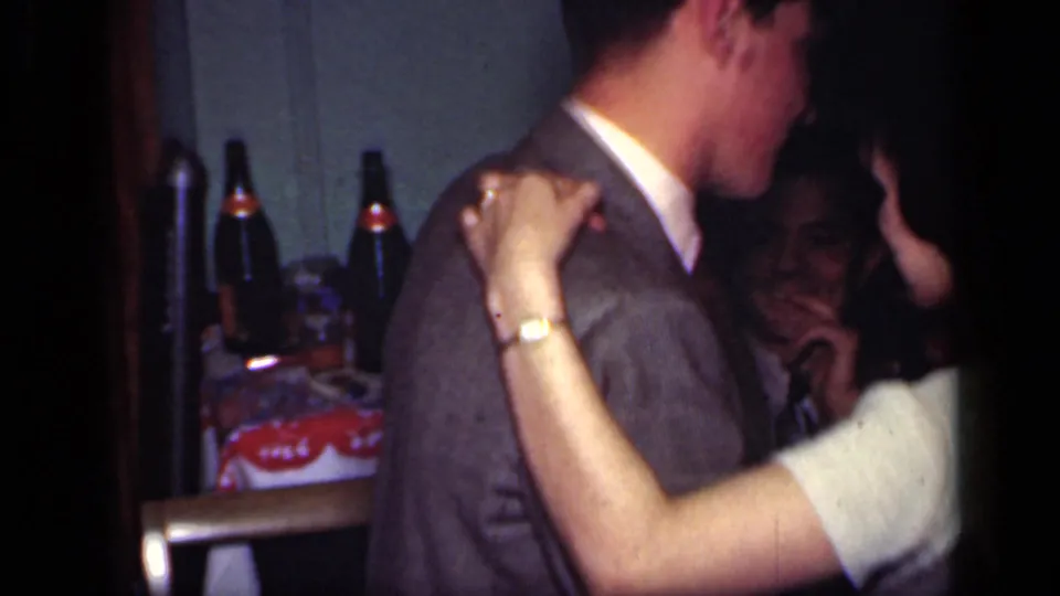 The couple dances closely beside a table with bottles in the background during the indoor 1949 New York gathering.