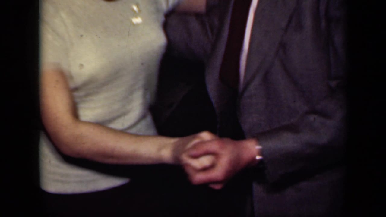 A close view shows a woman in a light shirt clasping hands with a suited dance partner in the 1949 New York interior footage.