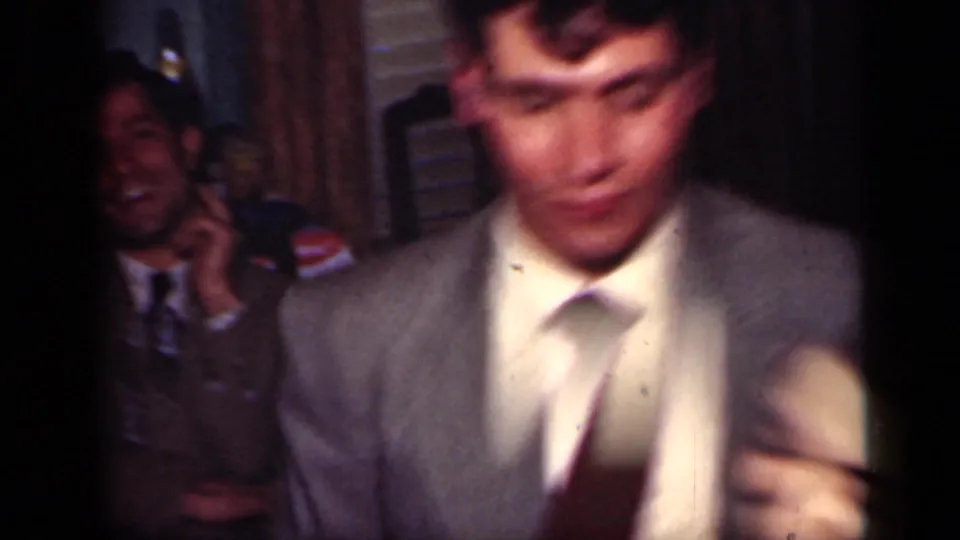 A suited man crosses the foreground while a seated onlooker smiles in the background of the 1949 New York home-movie dance scene.