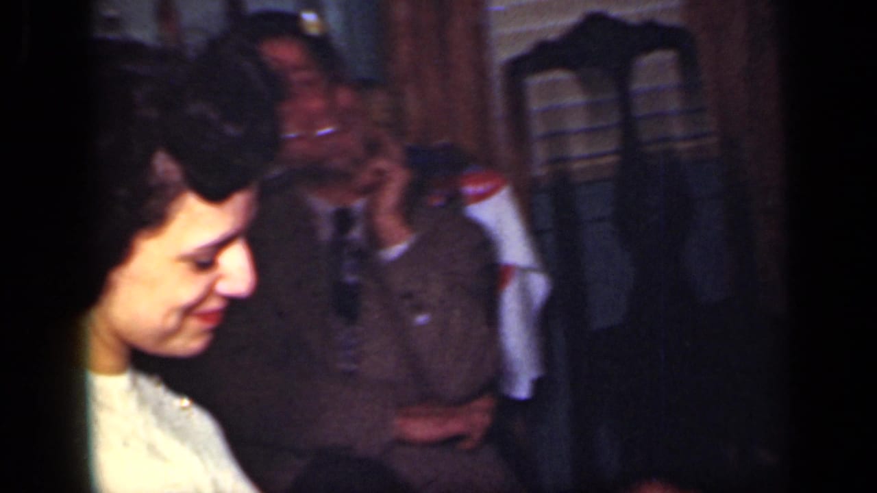 Young woman smiles beside seated guests in a dim indoor gathering.