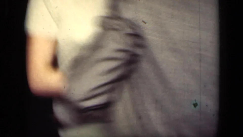 A blurred 1949 New York home-movie frame shows a light-dressed dancer moving beside a gray-suited adult in a private interior.