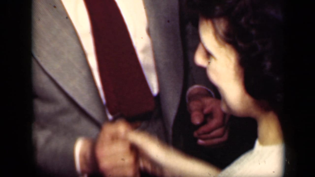 In 1949 New York home-movie footage, a woman in a light dress holds hands with a man in a gray suit during a close dance.