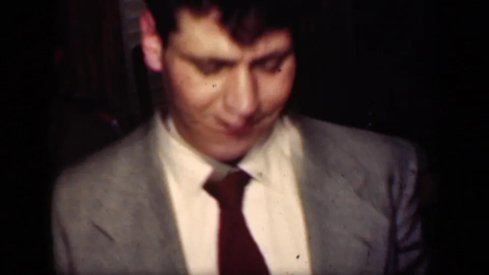 A man in a light gray suit and dark red tie appears in soft-focus 1949 New York home-movie footage during a dance or night out.