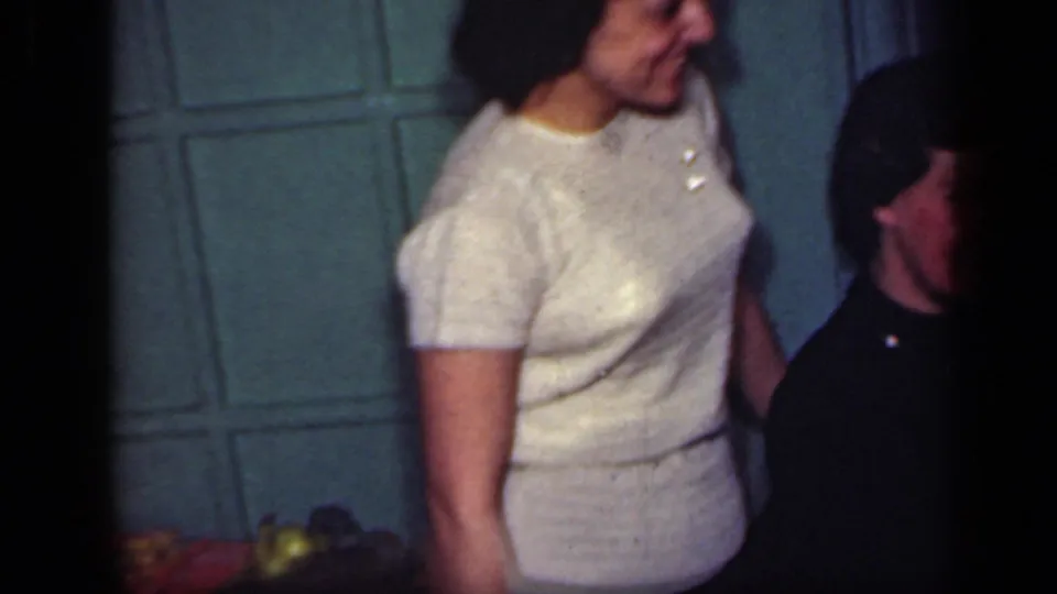 1949 New York home-movie frame with a woman in a light sweater and another adult standing together inside a painted room.