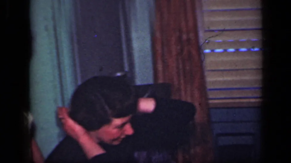 1949 New York home-movie frame showing an adult bending near a curtained window, blinds, and painted interior doors.