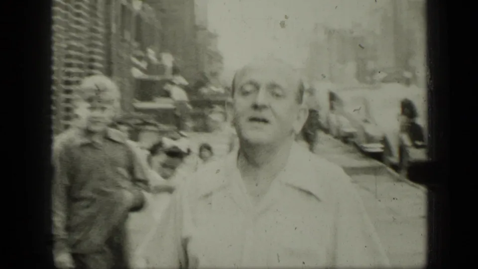 1949 New York home-movie frame in black and white showing a man close to camera with pedestrians and buildings behind him.