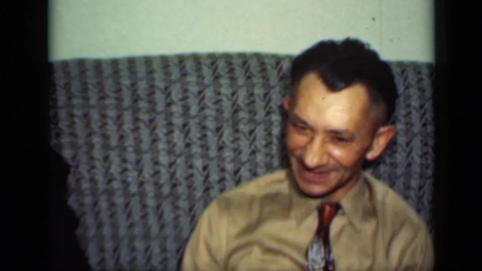 The man in a light shirt and patterned tie smiles warmly in the New York home-movie scene.