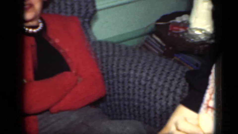 The woman sits back with crossed arms near a side table in a private New York interior, filmed on 8mm in 1949.