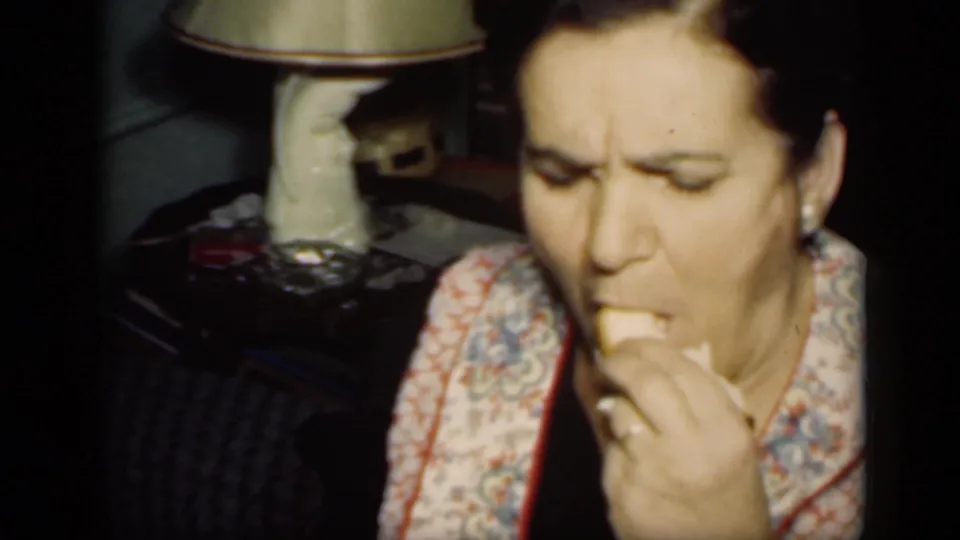 A woman in a patterned housecoat or jacket eats a small piece of food in a close interior 8mm shot from 1949 New York.