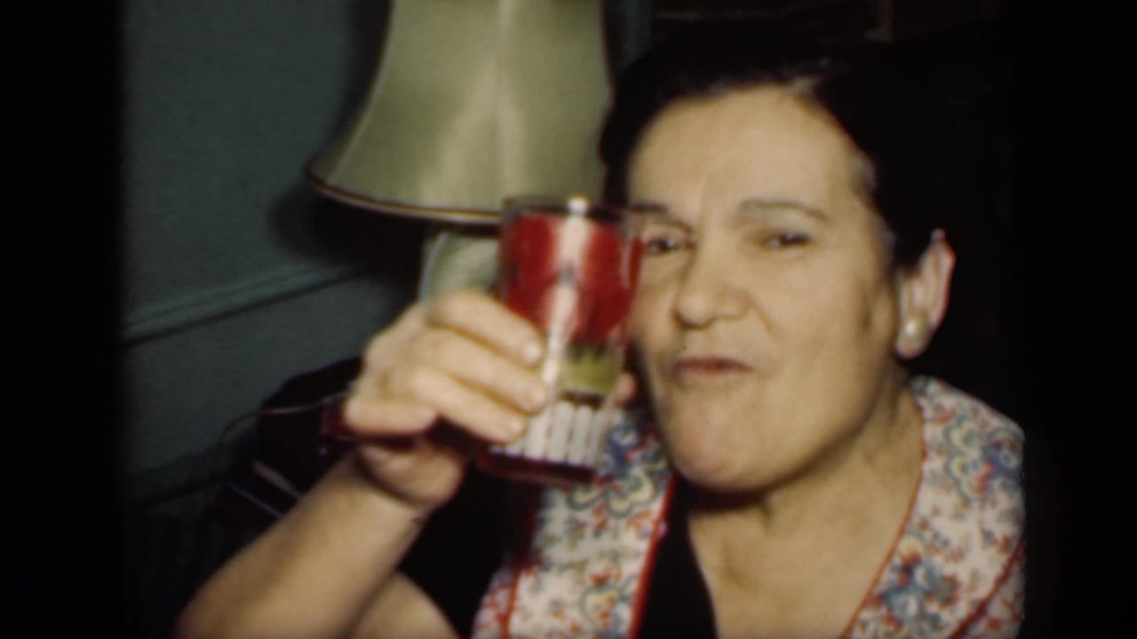 Adult woman in a dark dress raises a red cup inside a dim room.