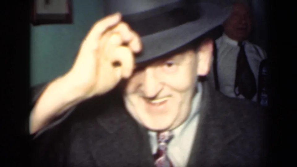 The 1949 New York frame shows the man smiling and touching the brim of his fedora, with other adults visible behind him indoors.