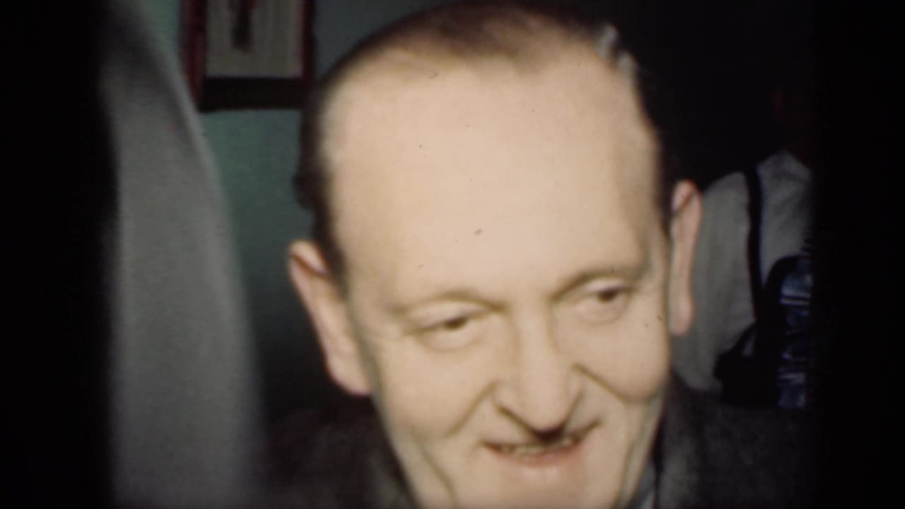 Smiling adult man in a suit seen close up inside a home.