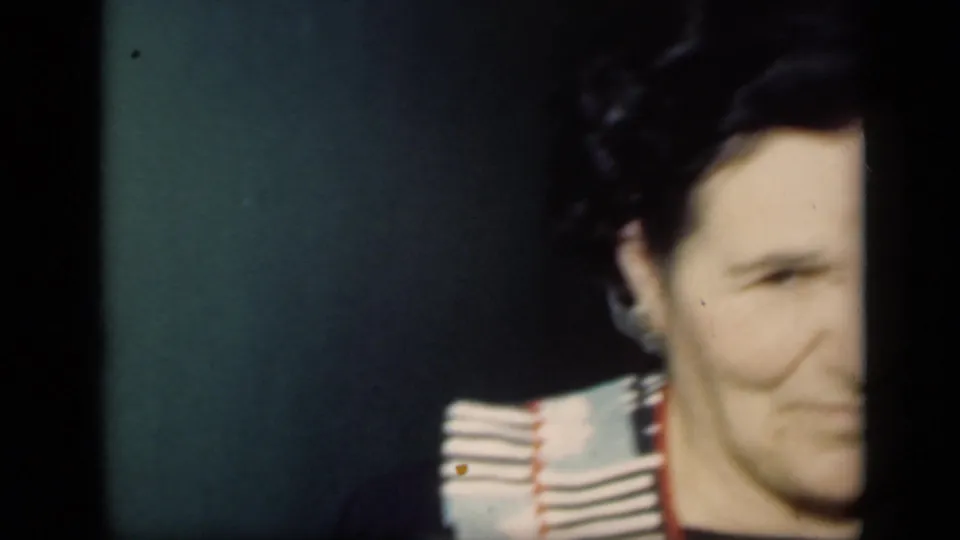 A dark-haired adult woman appears partly cropped in a close indoor frame from the 1949 home movie.