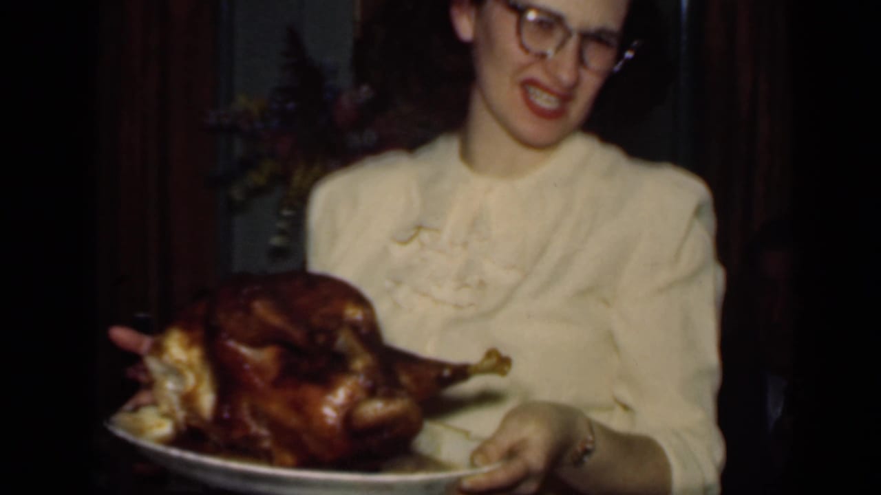 Woman smiles while angling a platter with a roasted turkey toward the camera.