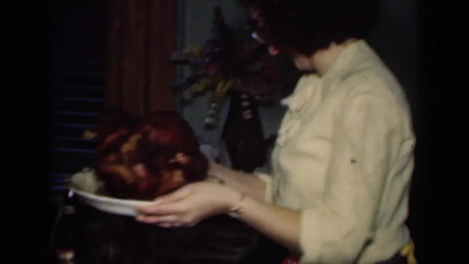 Side-profile frame shows the woman carrying the roasted turkey platter across a private New York home interior in 1949 footage.