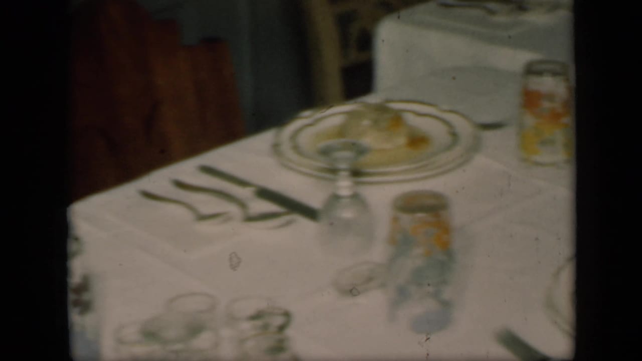 Formal dining table with china plates, napkins, glasses, and jars on a white tablecloth.