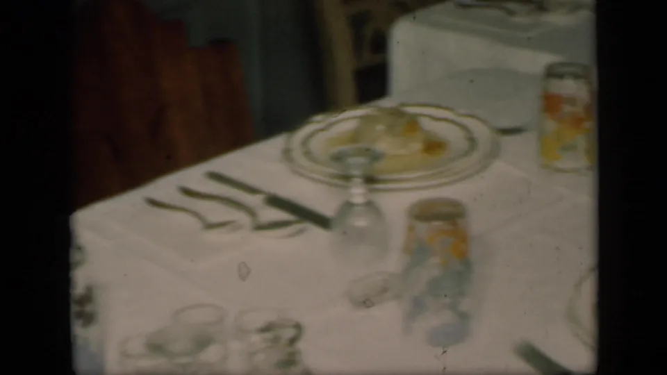 1949 New York home-movie frame showing a formally set dinner table with china plates, folded napkins, stemware, and small jars.