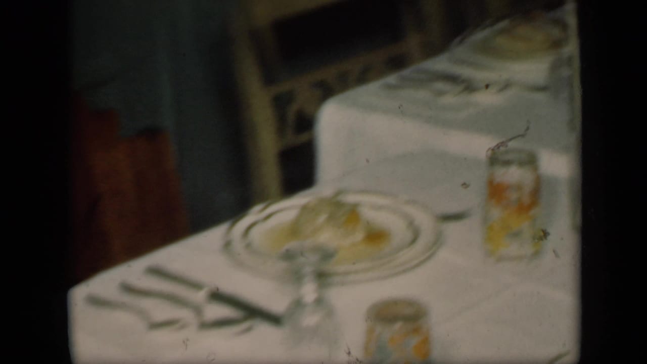 1949 New York home-movie frame with a slightly shifted view of the formal table setting, including plates, napkins, glasses, and jars.