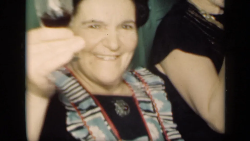 1949 New York home-movie frame of a smiling woman in a patterned dress raising her hand toward the camera in a private interior.