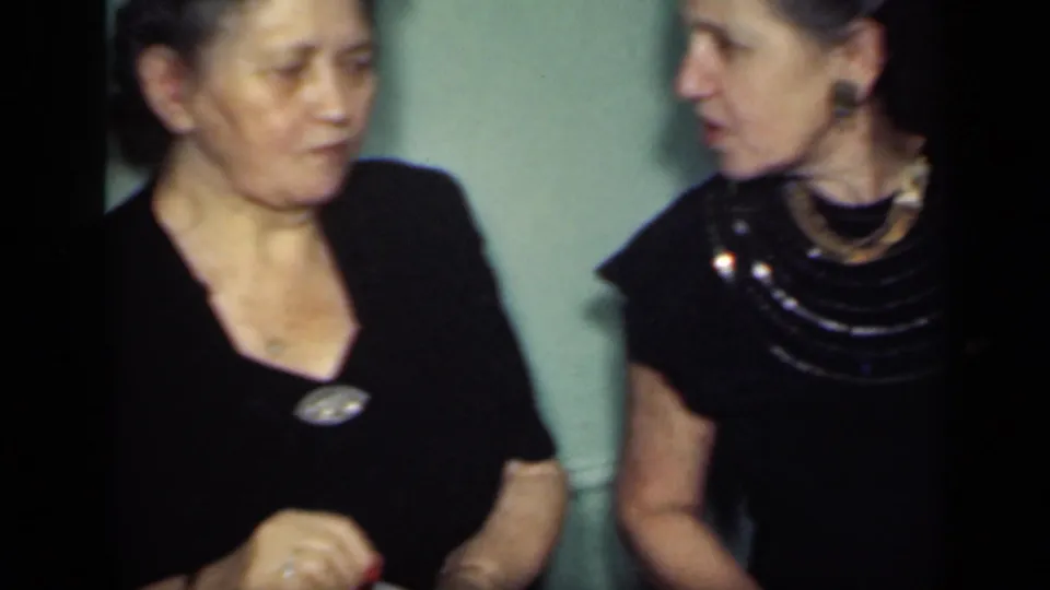 Two adult women in dark dresses appear to converse beside a green interior wall in 1949 New York home-movie footage.