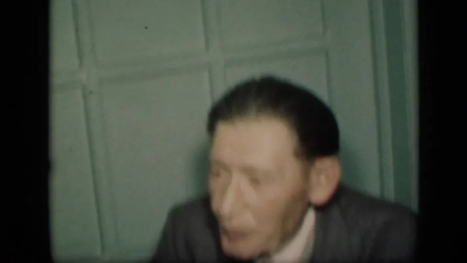 A soft-focus shot shows an older man in a dark suit seated before a green paneled wall, likely in the same indoor setting.