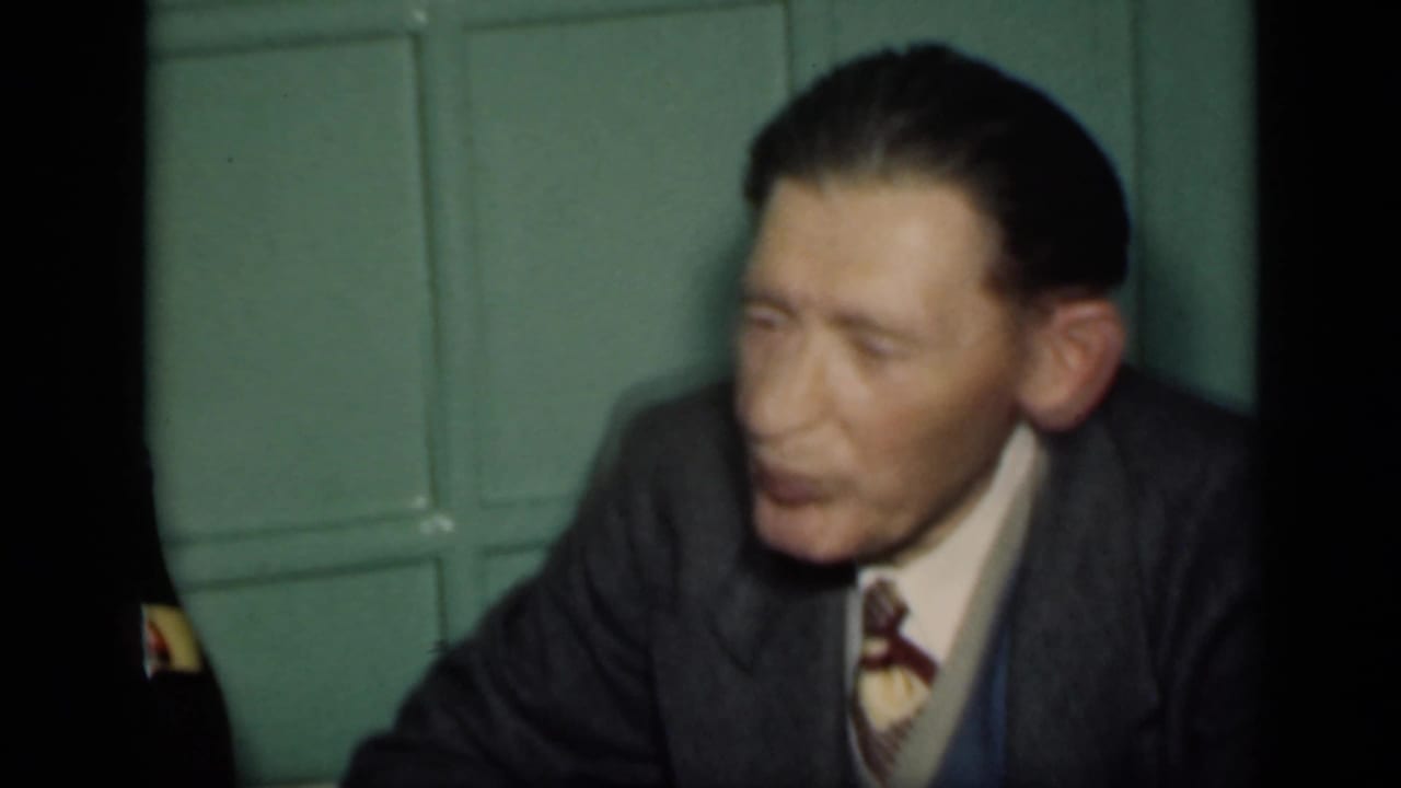 Seated man in suit before a green paneled wall.
