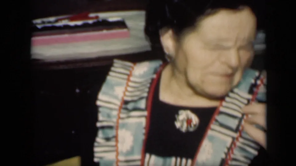 In the 1949 New York clip, a dark-haired woman wearing a ruffled apron frowns strongly while seated near a candy box indoors.