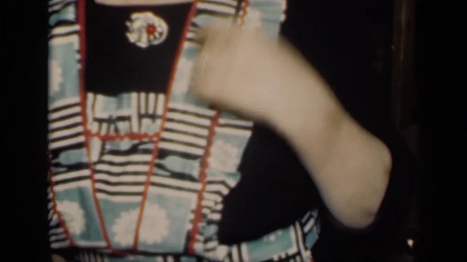The 1949 New York home-movie frame shows the woman's ruffled apron and raised arm, with her face mostly out of view in the interior.
