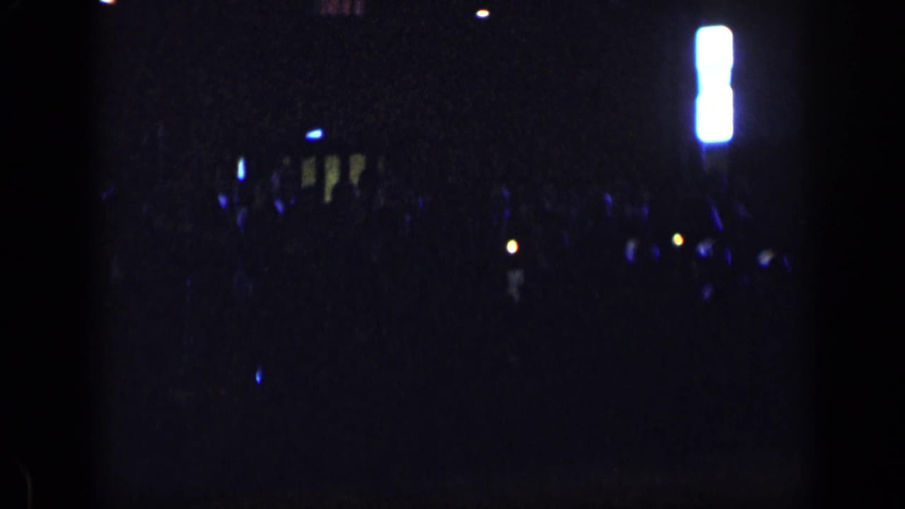 Dim 1957 New York indoor gathering with scattered blue highlights, distant figures, and a bright vertical fixture on the right.