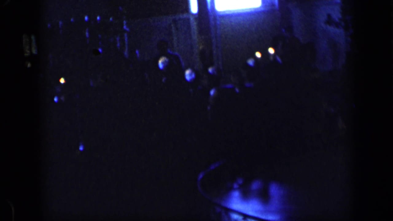 Very dark street view with scattered lights, silhouetted people, and a blue-lit foreground shape.