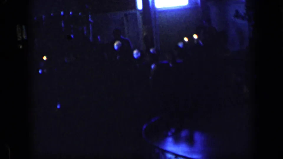 1957 New York night frame with indistinct people in deep shadow, small points of light, and a blue-lit area near the lower edge.