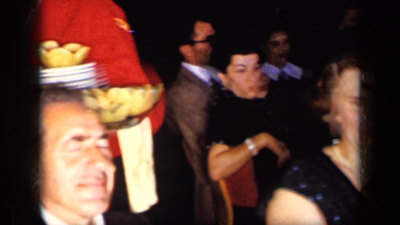 Waiter in red jacket holds a tray of bread rolls near dancing banquet guests.