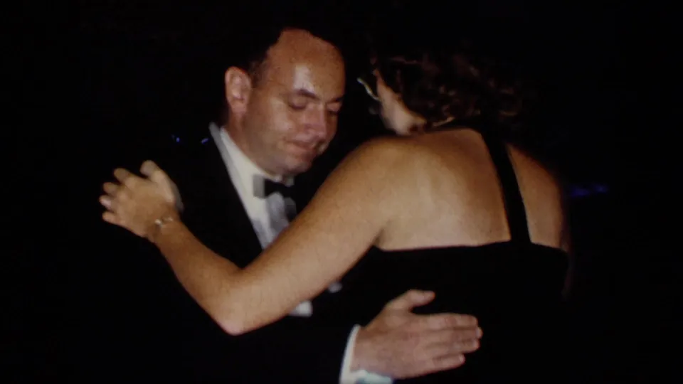 1957 New York banquet dance with a tuxedoed man and woman in a black dress dancing closely in low light.