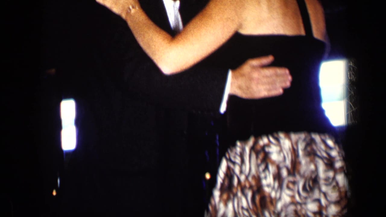 Partial view of a dancing couple, with arms and patterned skirt visible against a dark background.
