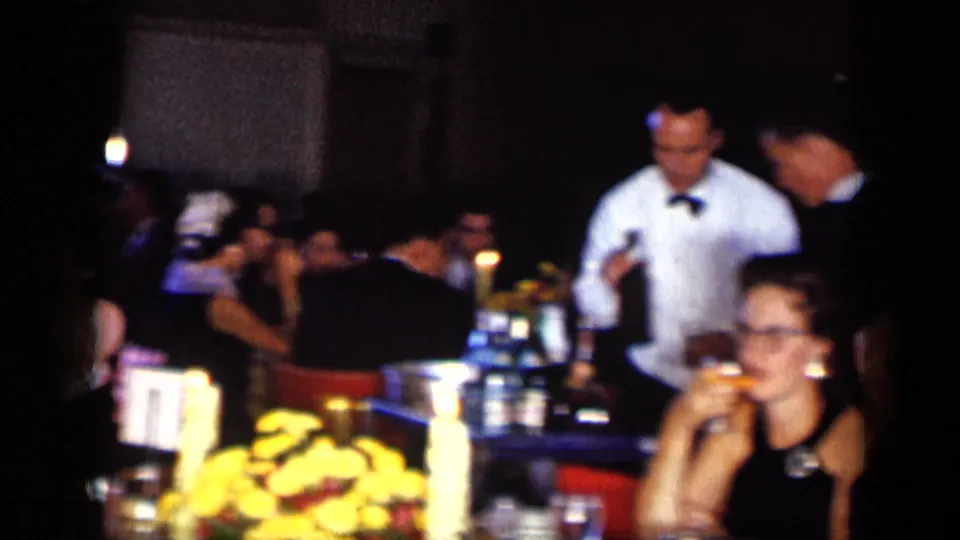 A crowded 1957 New York restaurant or bar scene shows guests at tables, a waiter in white, drinks, and bright flowers in the foreground.