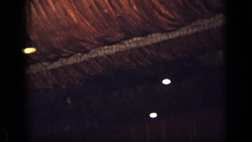 1957 New York 8mm frame emphasizing the straw-like ceiling pattern and several warm points of light in a shadowed interior.