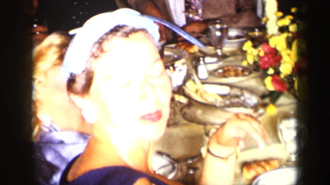 Woman in a blue headscarf seated at a dinner table with food and flowers.