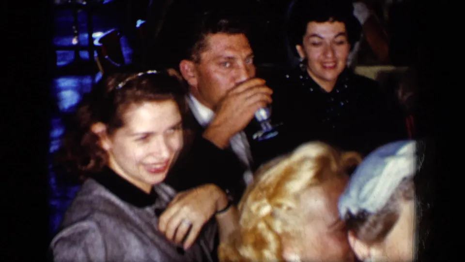 Candid 1957 New York home-movie frame of formal dinner guests smiling and drinking at a crowded table.